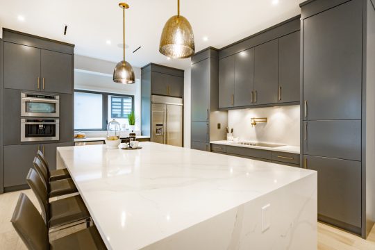 moderns virtuves interjers ar tumši zaļiem skapīšiem un salu no dabīgā akmens.