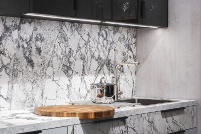 Virtuves darba virsma un sienas panelis no baltas akmens virsmas ar pelēku dzīslojumu.