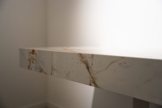 Gaiša Dekton virsma ar marmora dzīslu rakstu, biezu taisnu priekšmalu un precīzu vertikālo salaidumu.